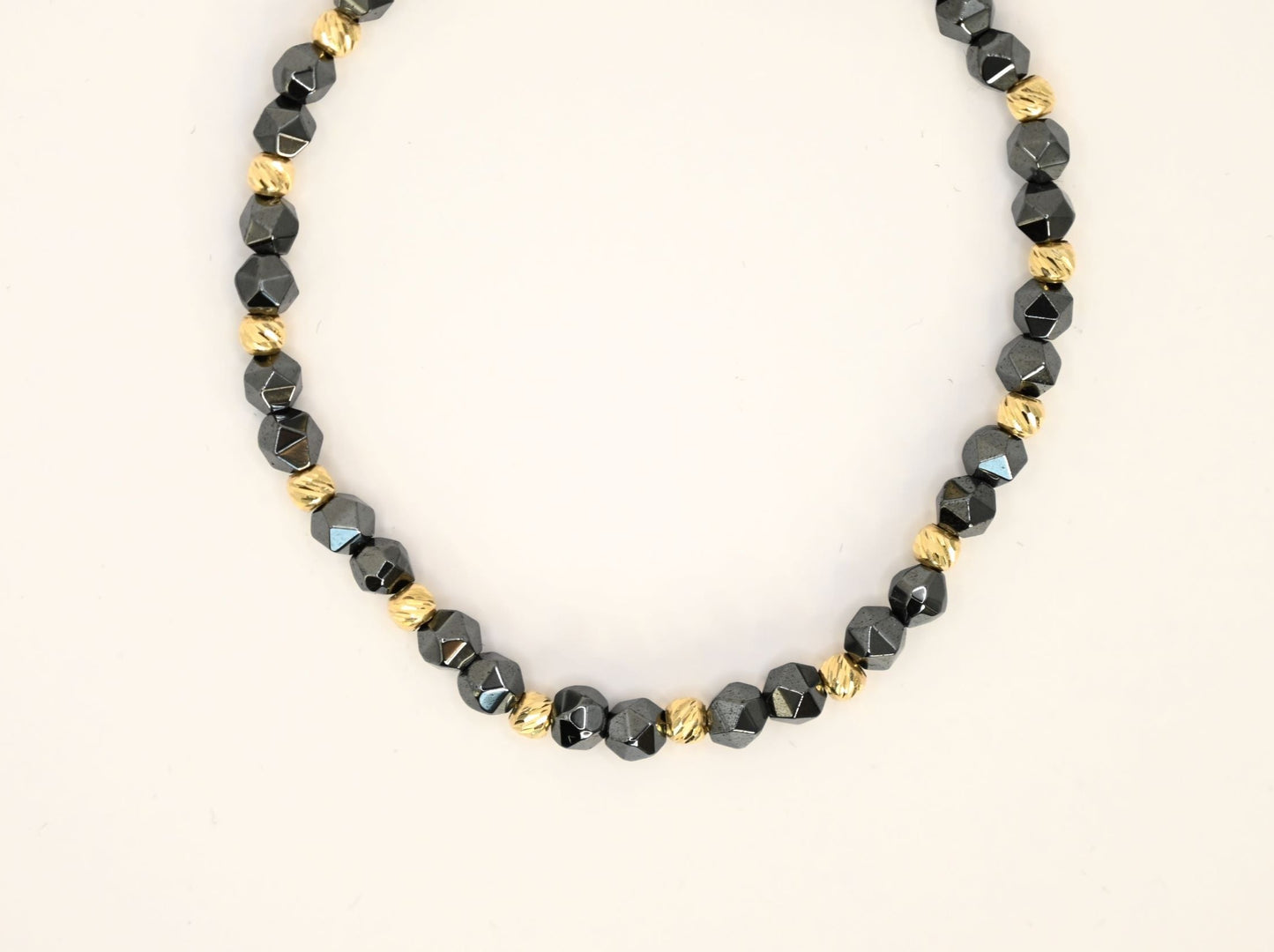 Een unisex kralenarmband met keramische kralen in antracietkleur en 14 karaat gouden kralen.