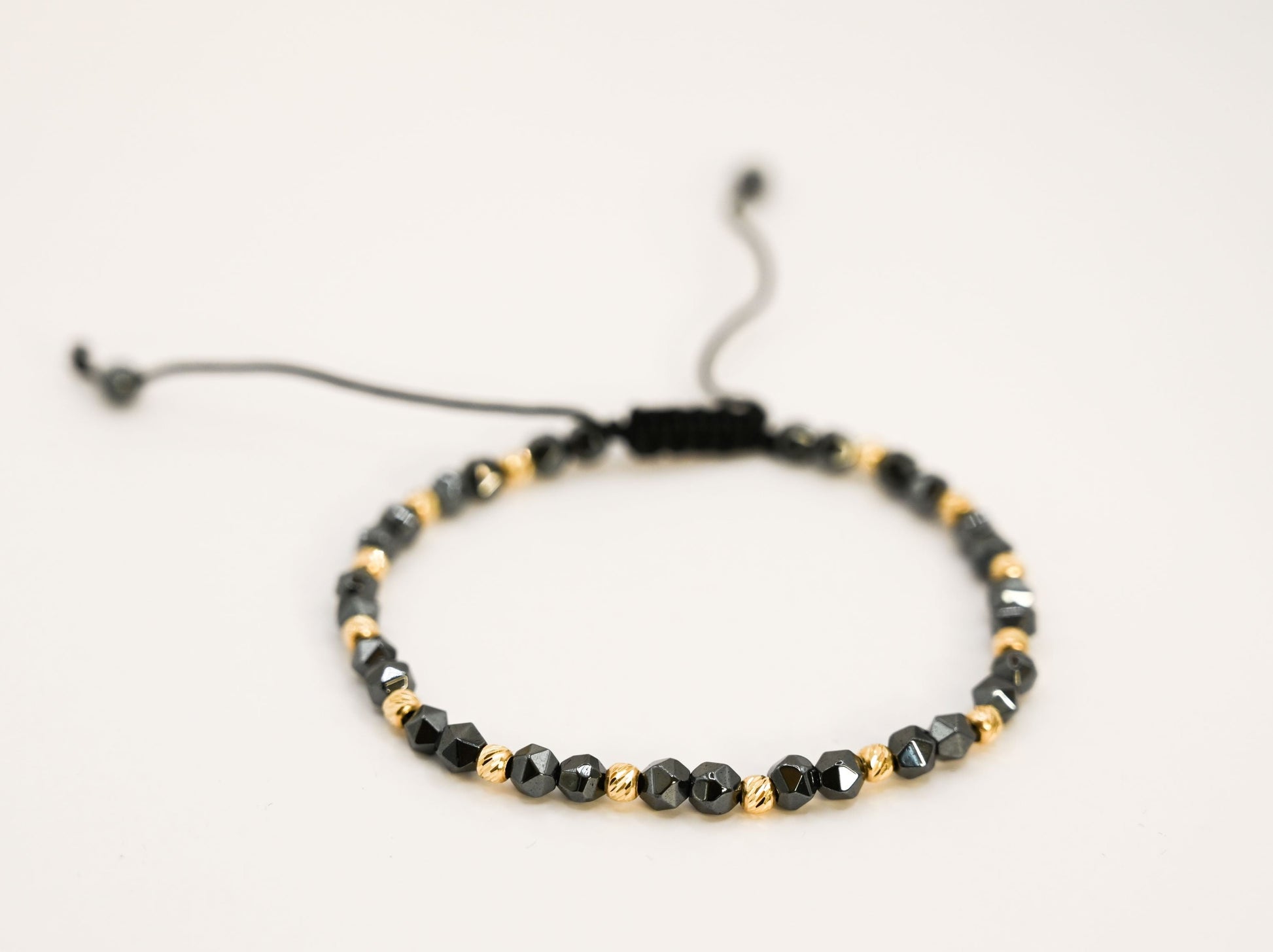 Een unisex kralenarmband met keramische kralen in antracietkleur en 14 karaat gouden kralen.