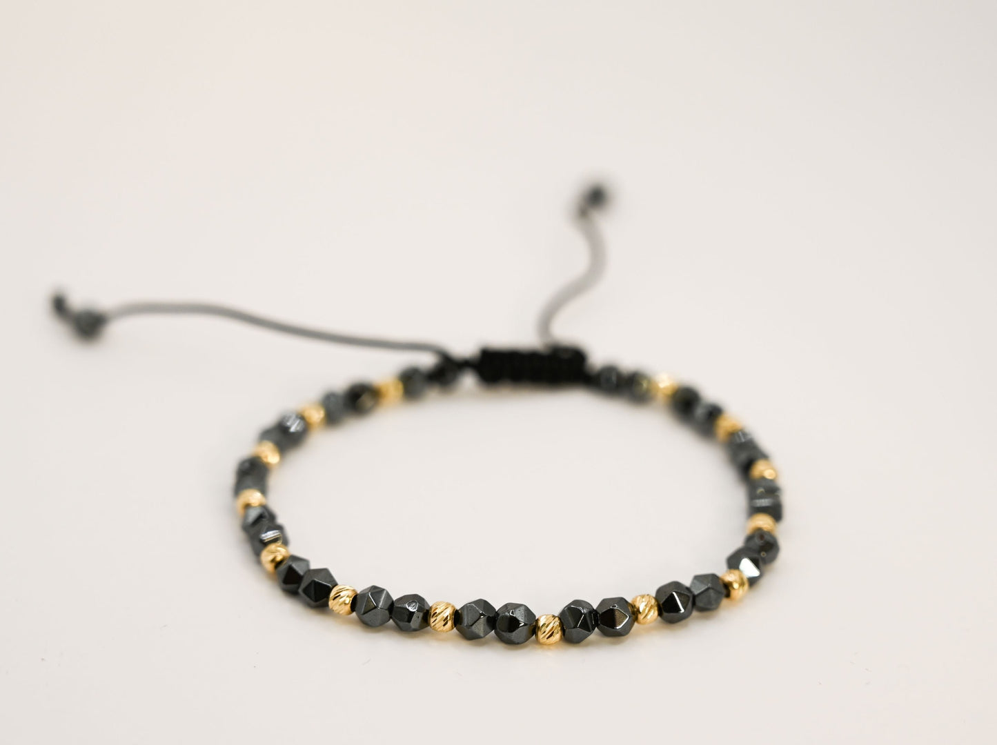 Een unisex kralenarmband met keramische kralen in antracietkleur en 14 karaat gouden kralen.