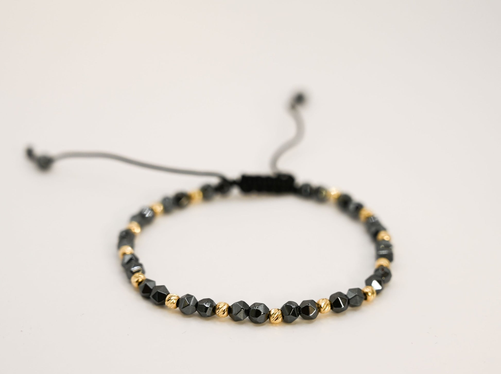 Een unisex kralenarmband met keramische kralen in antracietkleur en 14 karaat gouden kralen.
