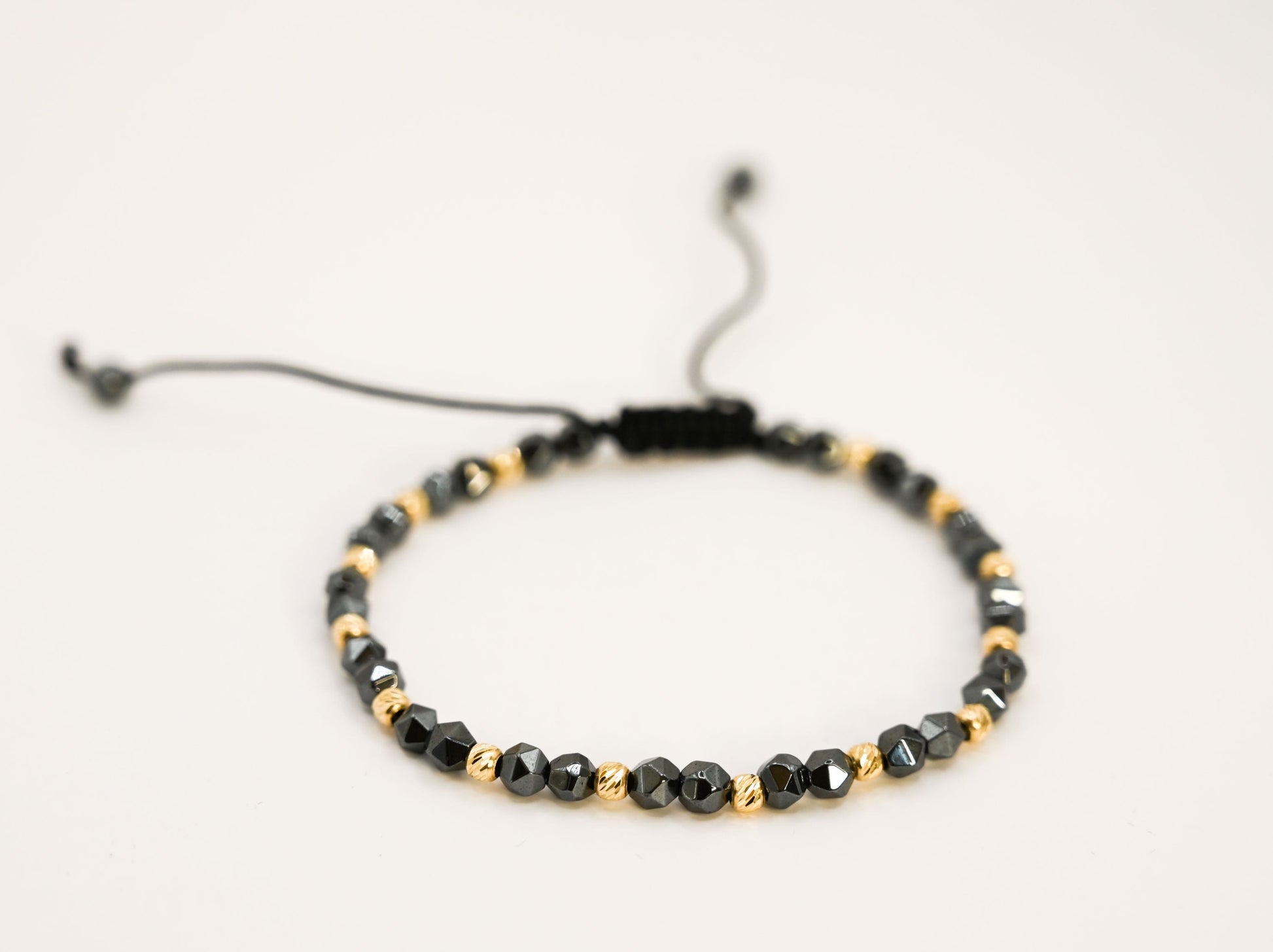 Een unisex kralenarmband met keramische kralen in antracietkleur en 14 karaat gouden kralen.